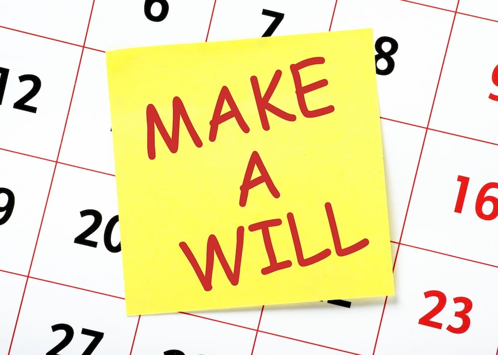Close up image of a calendar covered by a sticky note with the words, 'Make a Will' on printed on it.
