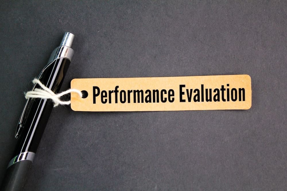 Image of a piece of paper with the words 'Performance Evaluation' printed on it. The paper is attached to the top of a ink pen with white string.